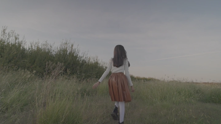 فتاة تسير في حقل أخضر عند الغروب، لقطة من الخلف.