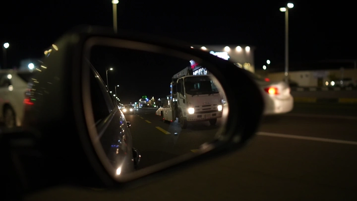 انعكاس سيارة في مرآة جانبية أثناء القيادة ليلاً، لقطة شارع.