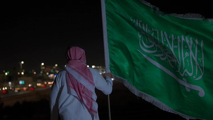 رجل يحمل العلم السعودي في الليل، منظر خلفي.