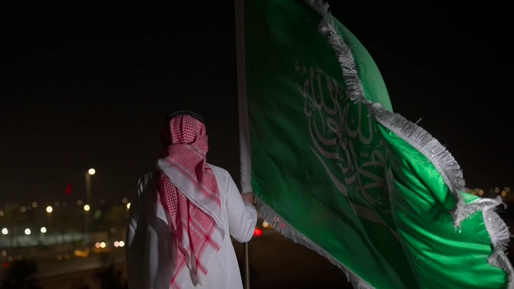 رجل يحمل العلم السعودي في الليل، لقطة خلفية.