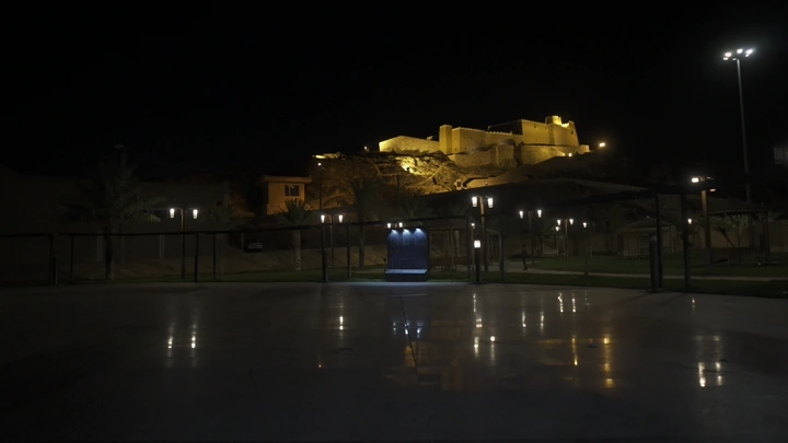 قلعة عيرف مضاءة ليلاً في حائل مع العلم السعودي، تصوير ليلي.