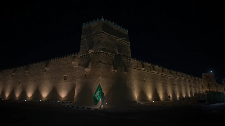 قلعة القشلة مضاءة ليلاً مع العلم السعودي في حائل، تصوير ليلي.