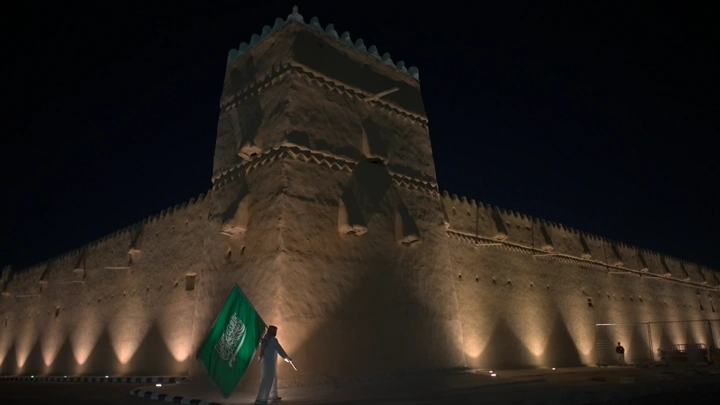 قلعة القشلة في حائل ليلاً مع العلم السعودي، لقطة ليلية.