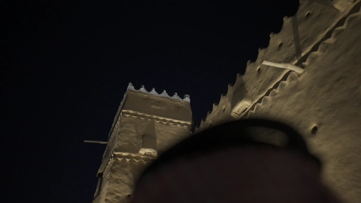 قصر القشلة مضاء ليلاً مع العلم السعودي في حائل، لقطة من الأسفل.