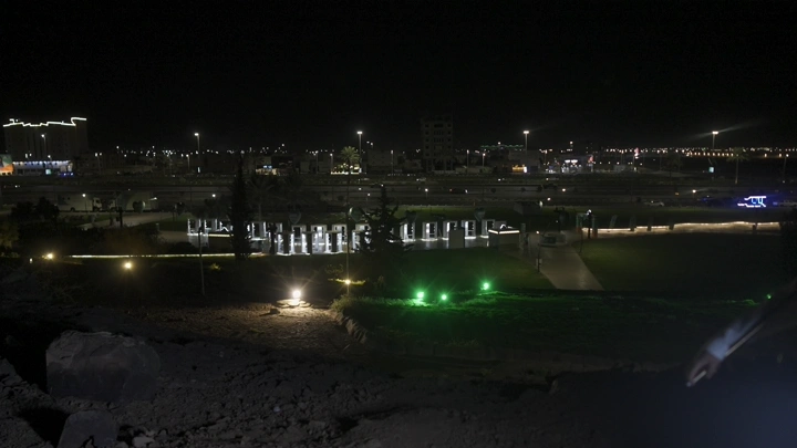 مدينة مضاءة ليلاً مع العلم السعودي، منظر ليلي.