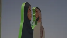 مجسمات لشخصين بزي سعودي وخلفهم تظهر سارية العلم السعودي، تصوير نهاري.