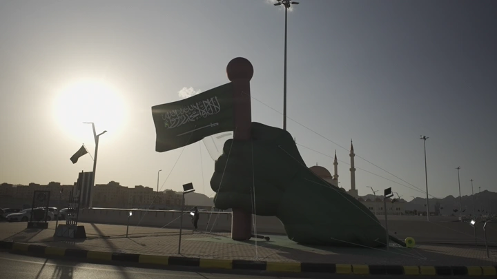 تمثال يد يحمل العلم السعودي في حائل عند الغروب، لقطة أرضية.
