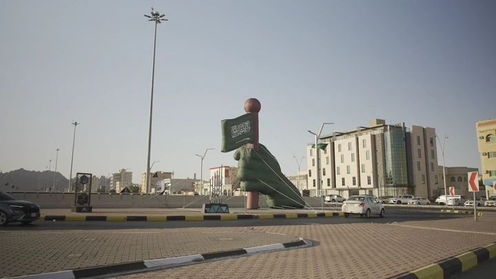 تقاطع مع تمثال يد تحمل علم السعودية في حائل، في يوم وطني، لقطة نهارية.