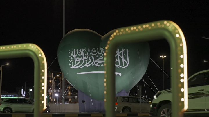 قلب أخضر كبير بشعار السعودية في الشارع ليلاً، لقطة ليلية.