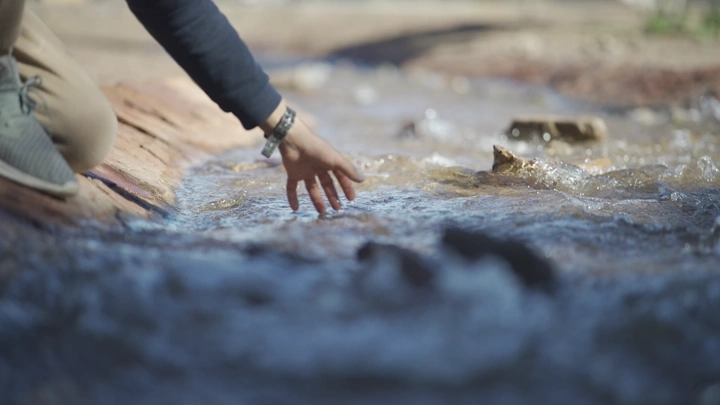 يد تلمس مجرى ماء في الطبيعة، لقطة قريبة.