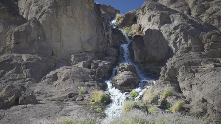 شلال صغير يتدفق بين الصخور في النهار، لقطة طبيعية.