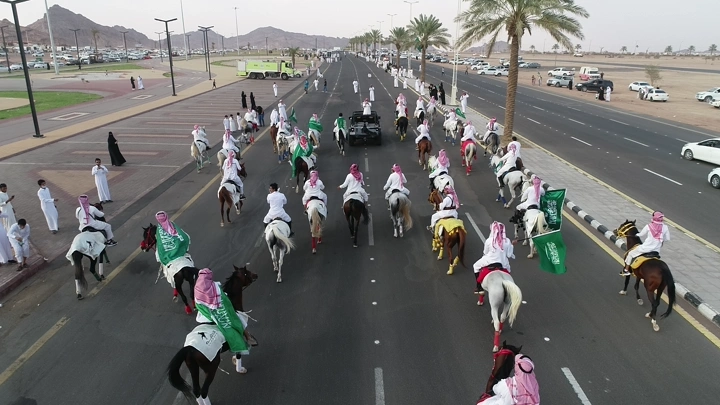 مسيرة خيول في اليوم الوطني السعودي على طريق واسع في حائل، لقطة جوية.