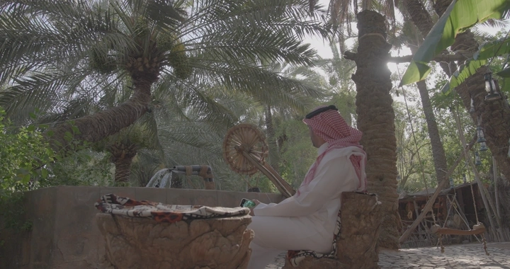 رجل يجلس بجانب ماطور ساقية في بستان نخيل، لقطة نهارية.