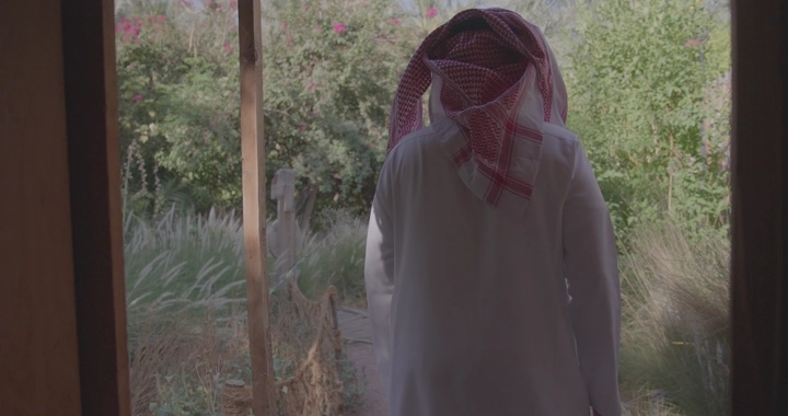 رجل يرتدي الزي السعودي في مزرعة، لقطة من الخلف.