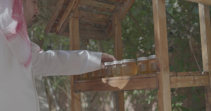 رجل يأخذ برطمان العسل من رف خشبي في الهواء الطلق، لقطة نهارية.