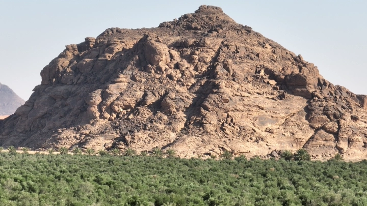 جبل صخري يطل على مزرعة خضراء، لقطة نهارية.