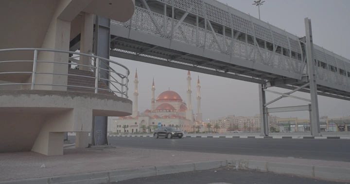 رجل يمشي تحت جسر مشاة مع وجود مسجد الراجحي حائل، لقطة نهارية.