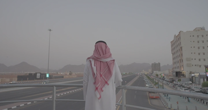 رجل يقف على جسر يطل على طريق الدائري في حائل، لقطة من الخلف.