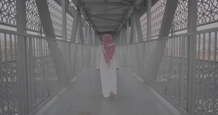 شخص يمشي على جسر مشاة معدني، لقطة من الخلف.