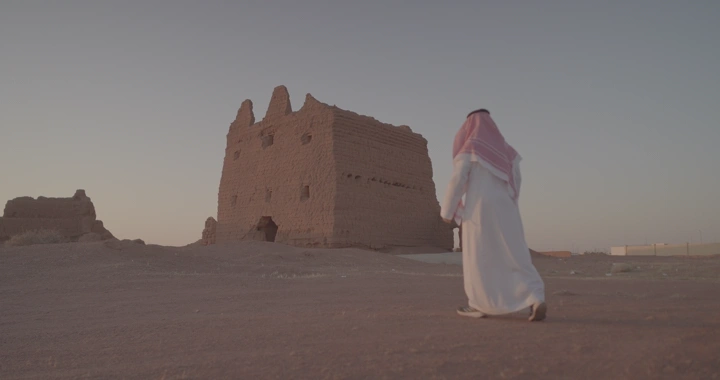 رجل يمشي نحو بيت طيني في الصحراء عند الغروب، لقطة واسعة.