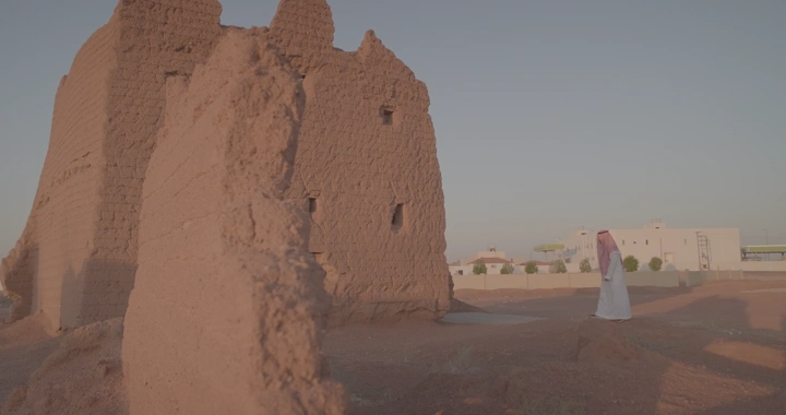 رجل يمشي إلى بيت طيني قديم في الصحراء، لقطة نهارية.
