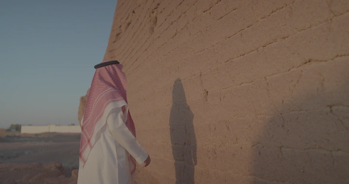 رجل بجانب جدار طيني في الصحراء يلمس الجدار، لقطة جانبية.