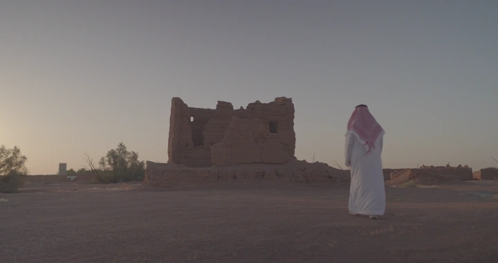 رجل يمشي نحو بيت طيني في الصحراء عند الغروب، لقطة واسعة.