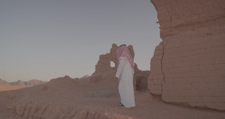 رجل بجانب بيت طيني قديم في الصحراء، لقطة واسعة.