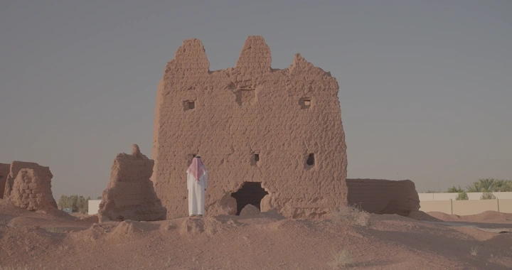رجل يقف عند بيت طيني قديم في الصحراء، لقطة نهارية.