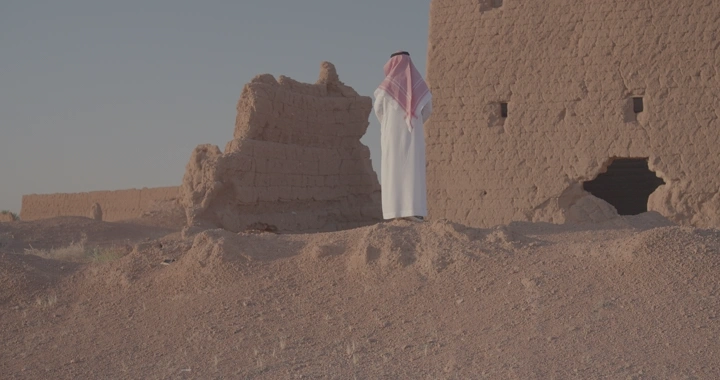 رجل بجانب بيت طيني في الصحراء، لقطة نهارية.