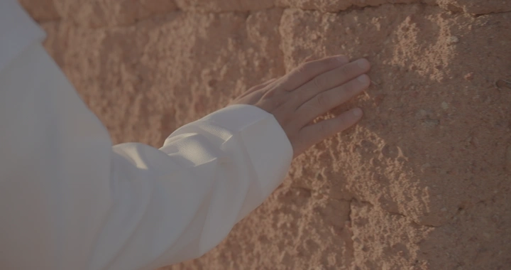 يد تلمس جدار طيني في ضوء النهار، لقطة قريبة.