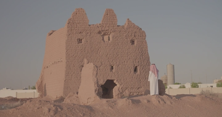 رجل يقف عند بيت طيني تقليدي في الصحراء، لقطة نهارية.