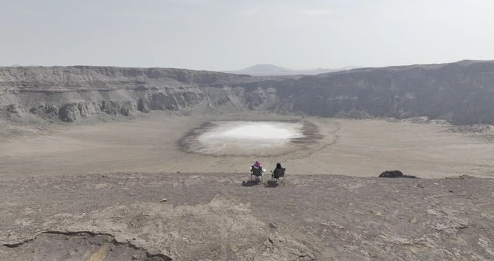 فوهة بركان الهتيمه في حائل، لقطة جوية تظهر شخصين يجلسان على الحافة.