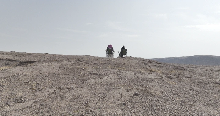 شخصان يجلسان على كراسي على حافة فوهة بركان الهتيمه في حائل، لقطة من الأرض.