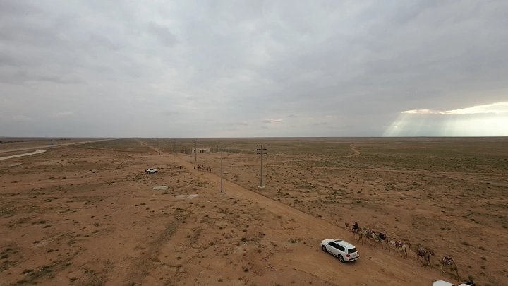 صحراء واسعة مع سيارات وجمال، لقطة جوية.