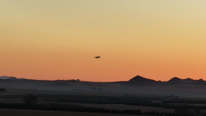 طائرة تحلق فوق تلال عند الغروب، لقطة من الأرض.