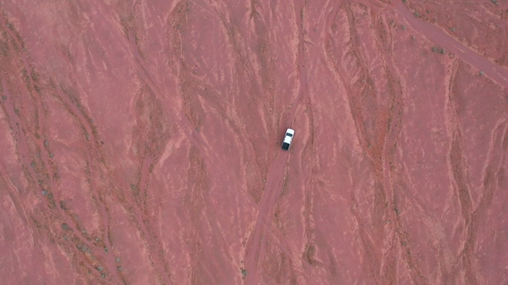 سيارة في صحراء حمراء من الأعلى، لقطة جوية اسقاطية.