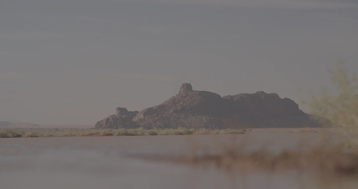 جبل في حائل مع بركة مياه بعد الأمطار عند الغروب، لقطة من الأرض.