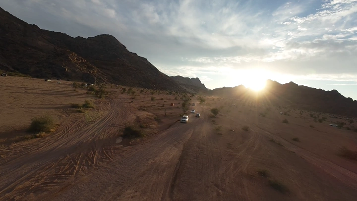 سيارات تسير في صحراء وجبال مشار في حائل عند الغروب، لقطة درون.