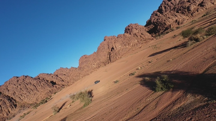 سيارة تسير على كثبان رملية بين جبال توارن حائل، لقطة درون.