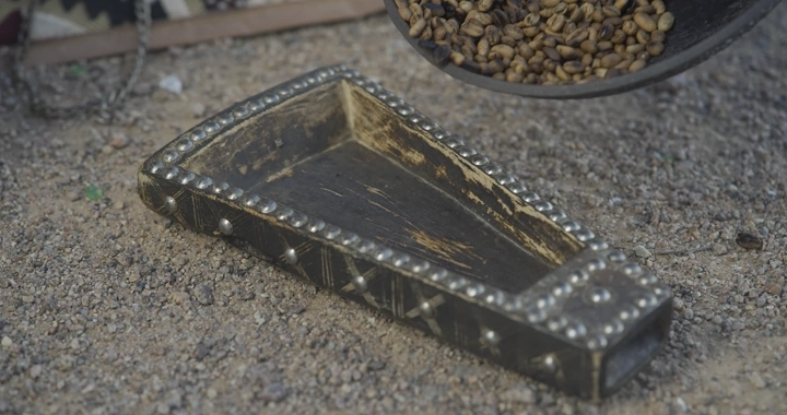 حبوب قهوة محمصة تسكب في وعاء تقليدي على الأرض، لقطة مقربة.