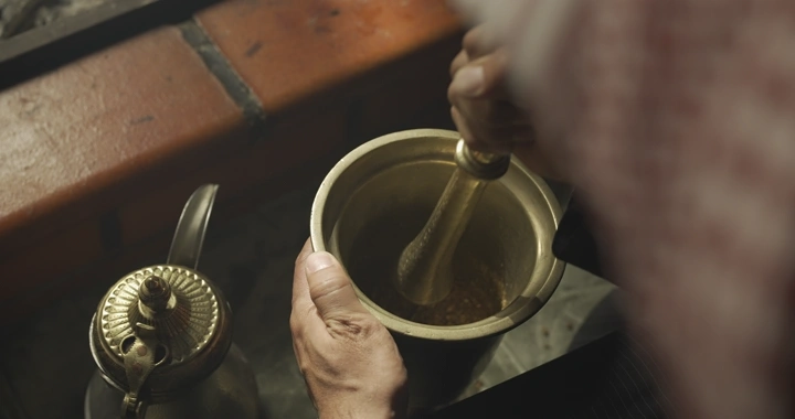 شخص يدق النجر بجانب دلة قهوة، لقطة قريبة.