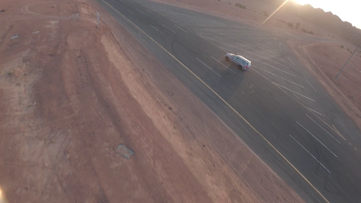 سيارة تسير على طريق صحراوي عند الغروب، لقطة جوية.