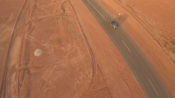 سيارة تسير على طريق صحراوي عند الغروب، لقطة جوية.