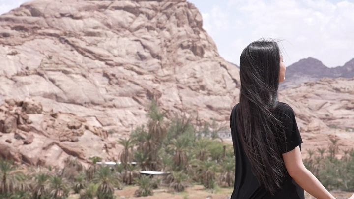 امرأة تتأمل الجبال في واحة صحراوية، لقطة جانبية.