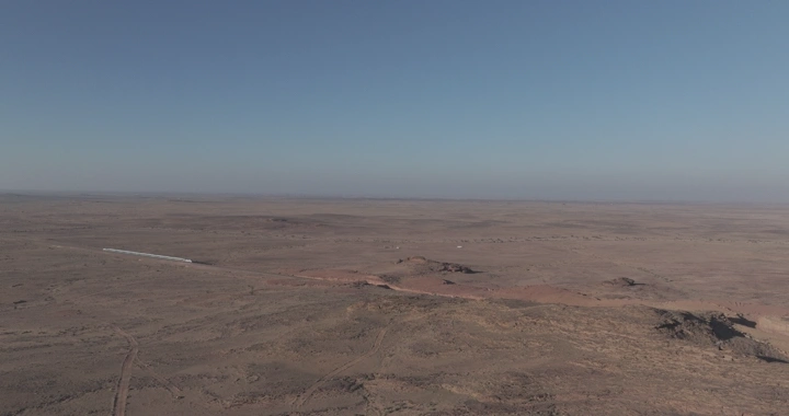 قطار يعبر صحراء شاسعة تحت سماء زرقاء، لقطة جوية.