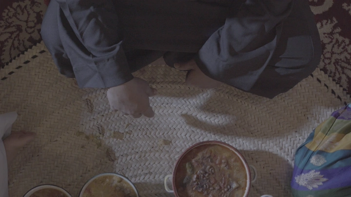 اكلات سعودية على حصير في غرفة المعيشة مع اجتماع العائلة على الغداء، لقطة علوية.