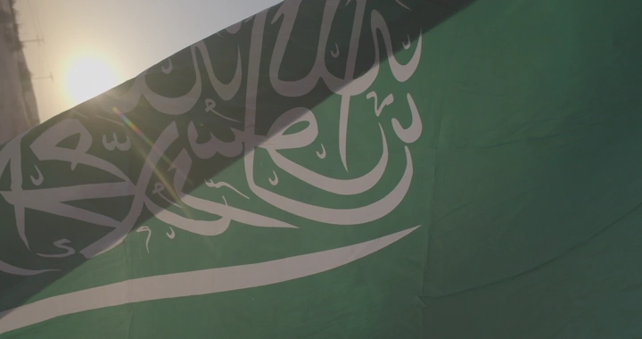 رجل يحمل علم السعودية في النفود مع شمس خلفه، لقطة جانبية.