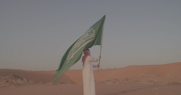 رجل يحمل علم السعودية في الصحراء، لقطة من الجانب.