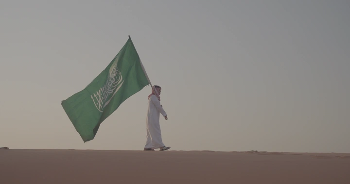 رجل يحمل علم السعودية في النفود، لقطة جانبية.